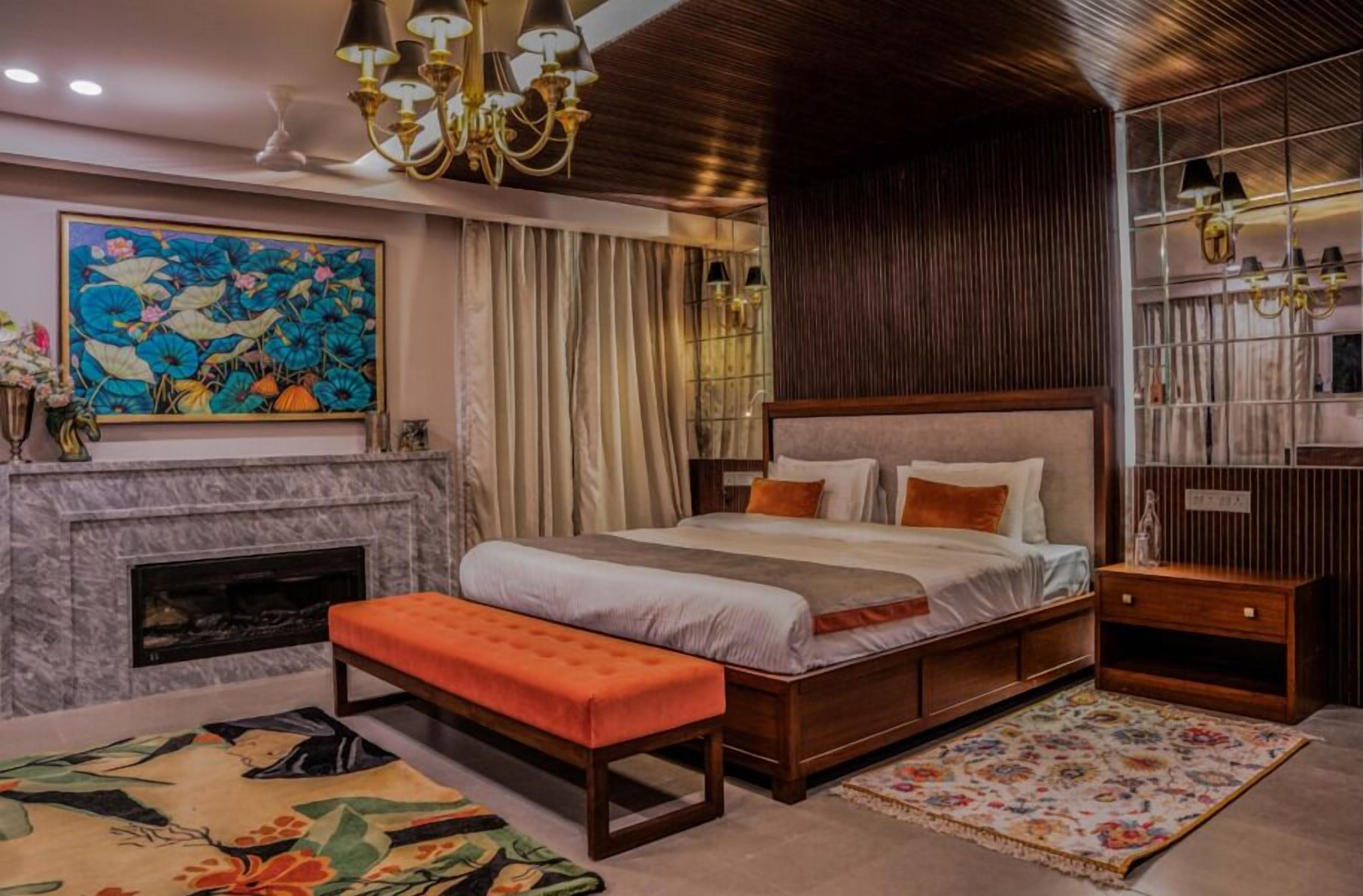 A bedroom with a large bed, a fireplace, a bench, a colorful rug, and a decorative painting.