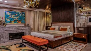 A bedroom with a large bed, a fireplace, a bench, a colorful rug, and a decorative painting.