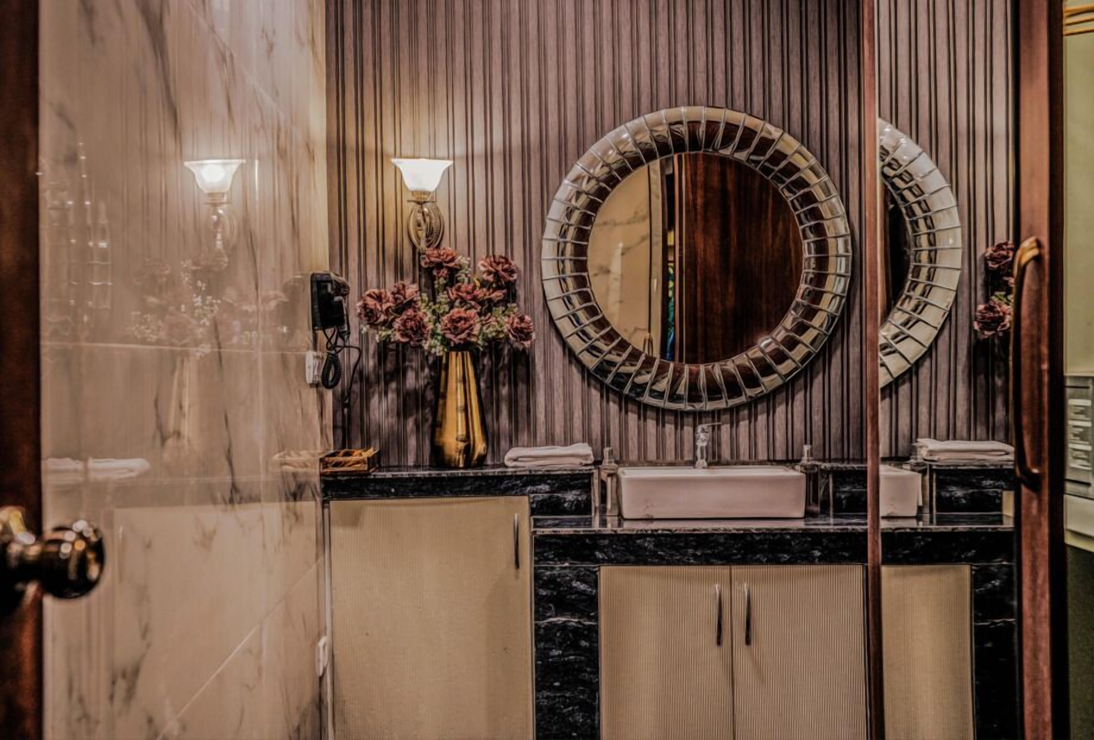 A bathroom with a marble vanity, two wall-mounted mirrors, a sink, and a vase with flowers.