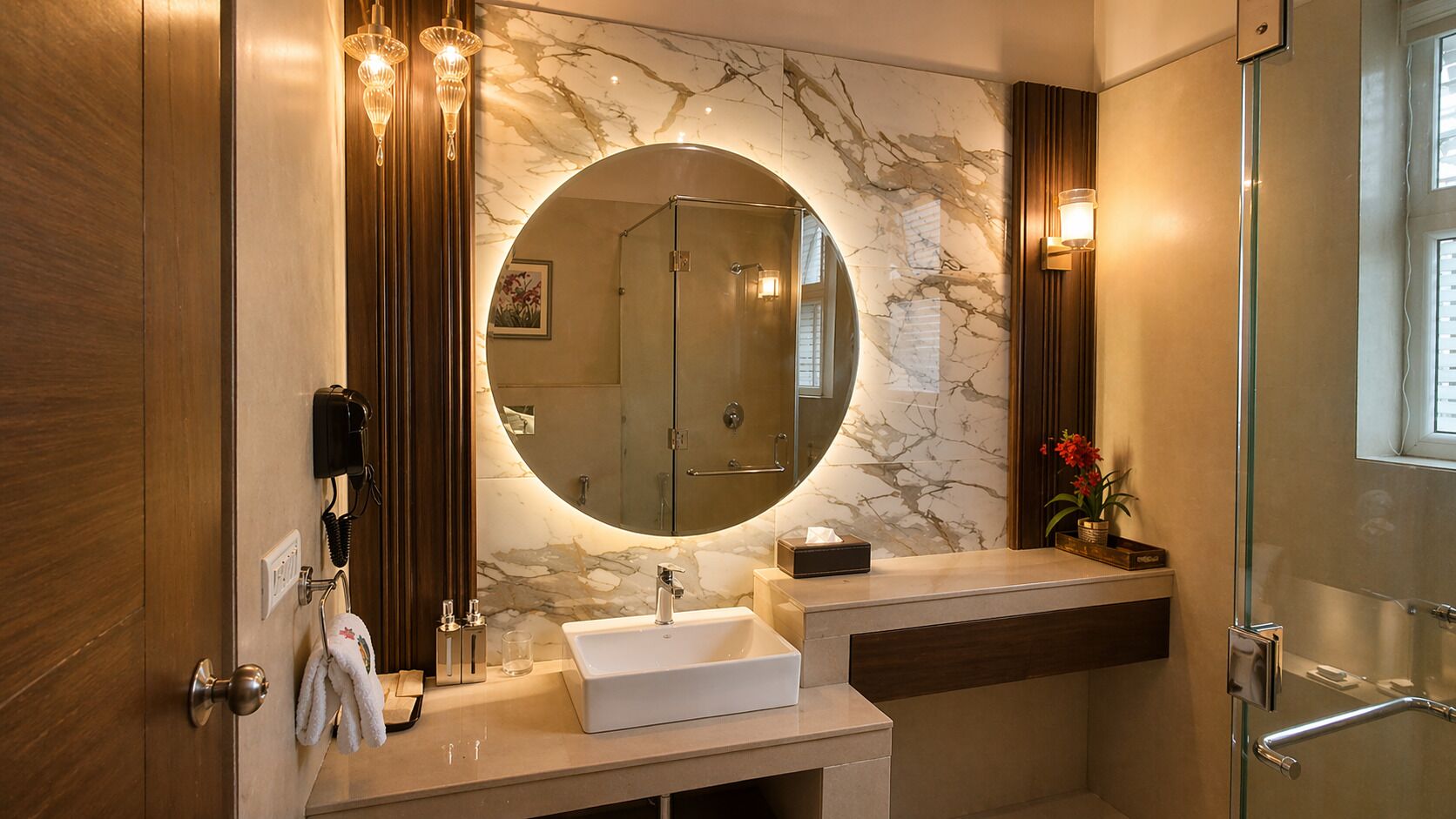 A bathroom with a marble wall, a round mirror, a sink, a shower, and a telephone.