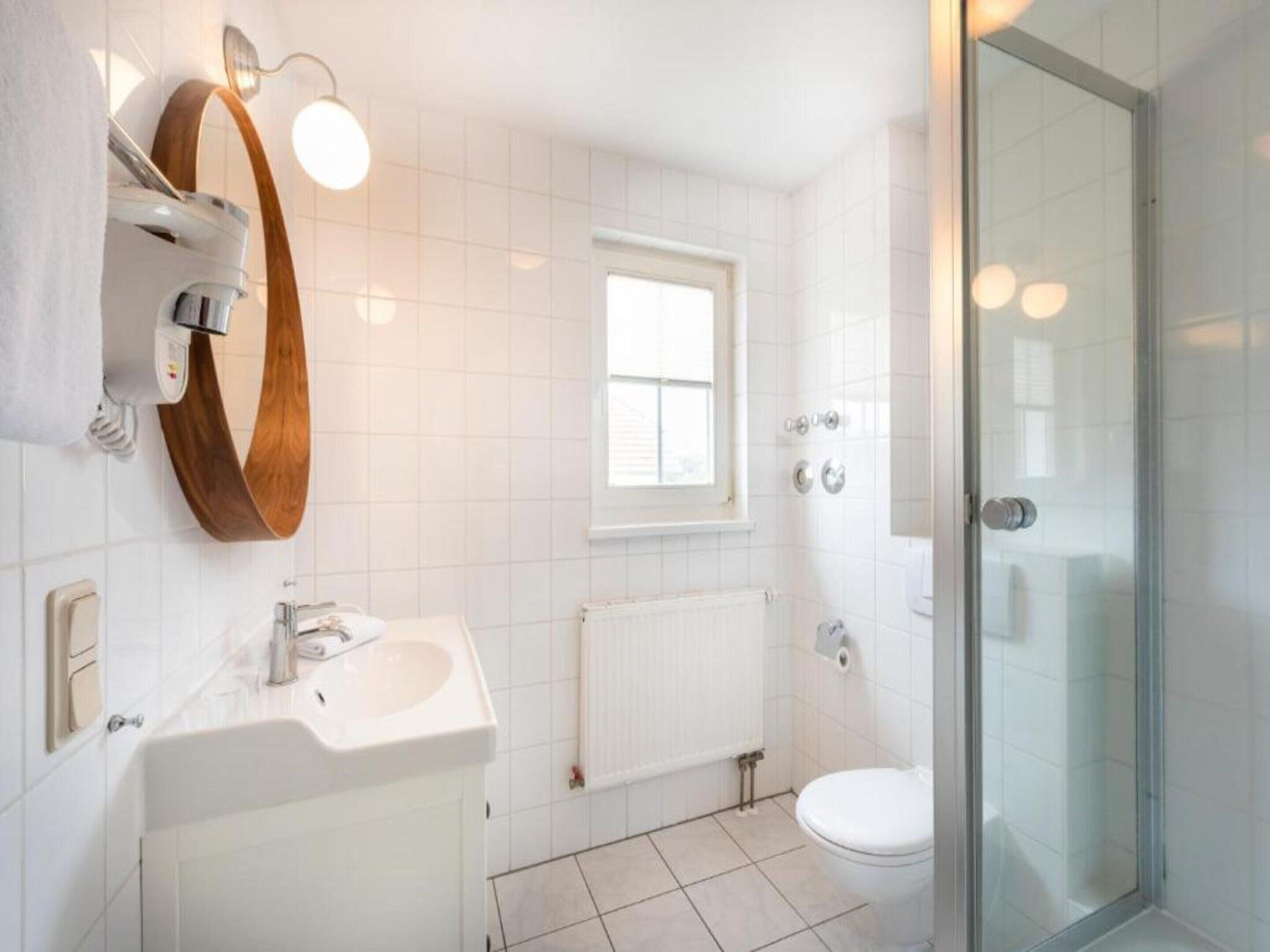 A modern bathroom with a white sink, a mirror, a toilet, and a glass shower enclosure.
