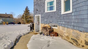 Una casa con un camino de entrada cubierto de nieve y una pila de leña afuera.