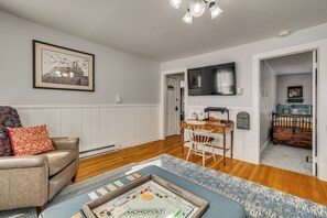 A living room with a sofa, a coffee table with a Monopoly game, a TV, and a door leading to a bedroom. - Easy Beach Access! New London Apt w/ Kitchenette (New London)