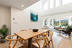 Amplia sala de estar con mesa de comedor de madera, sillas acolchadas, sofá y un ventanal con vistas a la montaña.