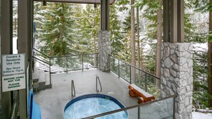 Bereich mit Whirlpool, Steinpfeiler, Holzbank und Hinweisschild mit Angaben zu den Spa-Öffnungszeiten.