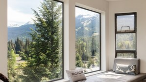 Ein Zimmer mit großem Fenster und Blick auf die Berge, einem Bett mit weißer Matratze und einem Kissen mit dem Aufdruck 'whistler' sowie einem kleinen Tisch mit Stuhl.