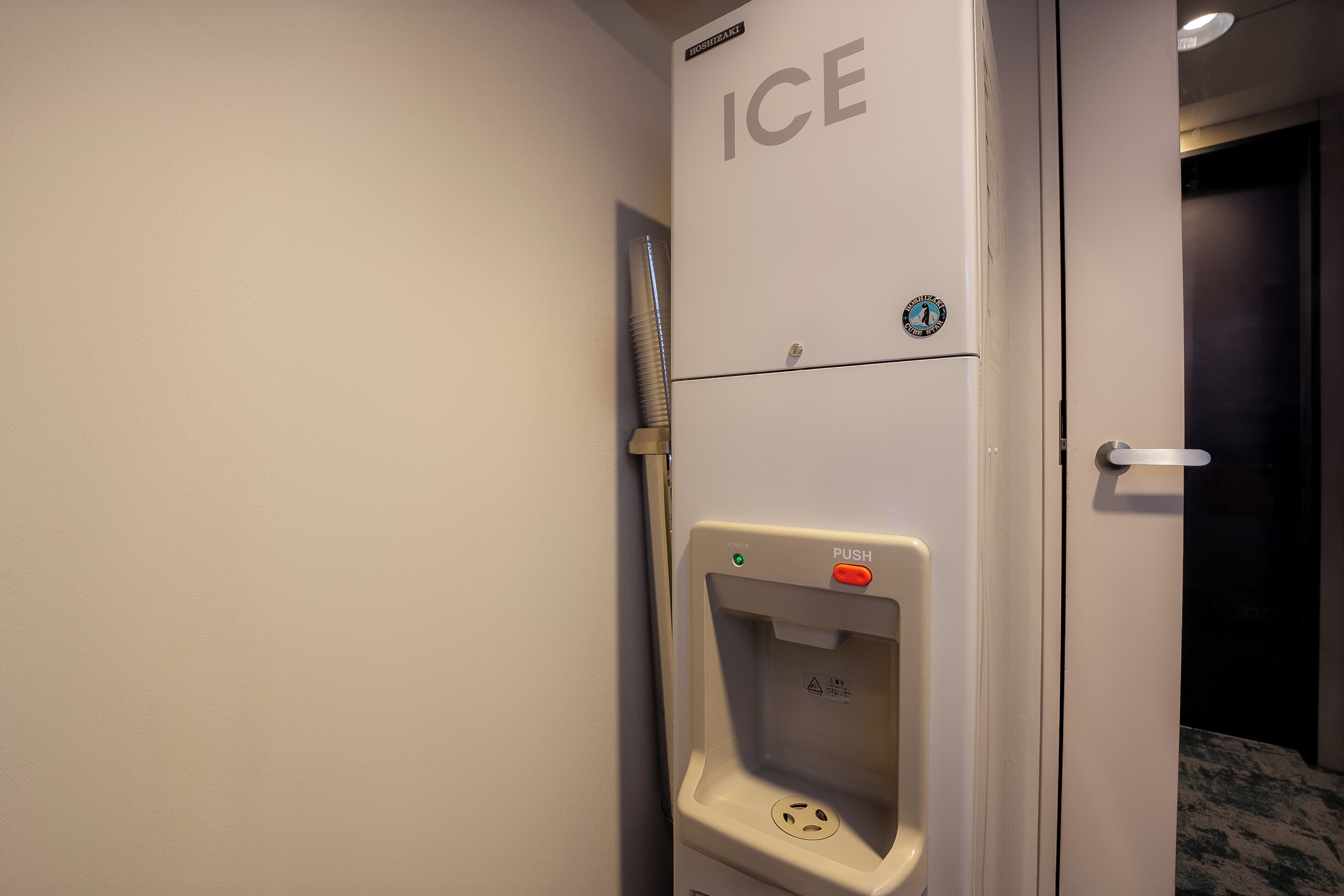 A hotel room with a white wall, a door labeled 'ICE,' and a push button for the ice dispenser.