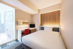 A hotel room with a large bed, a desk with a computer, a red chair, and a city view.