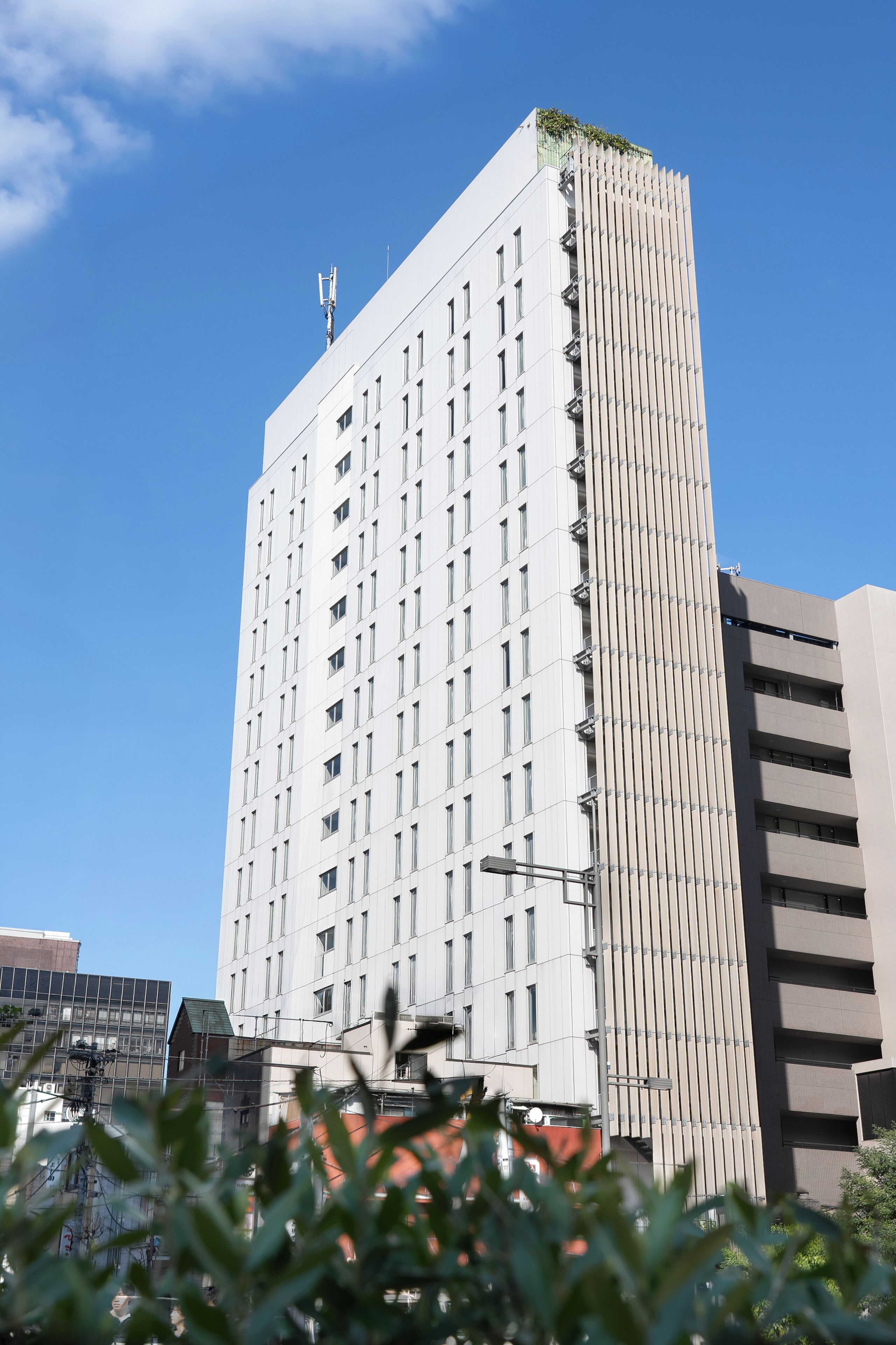 A tall, modern building with a grid of windows, a flat roof, and a visible antenna on top.