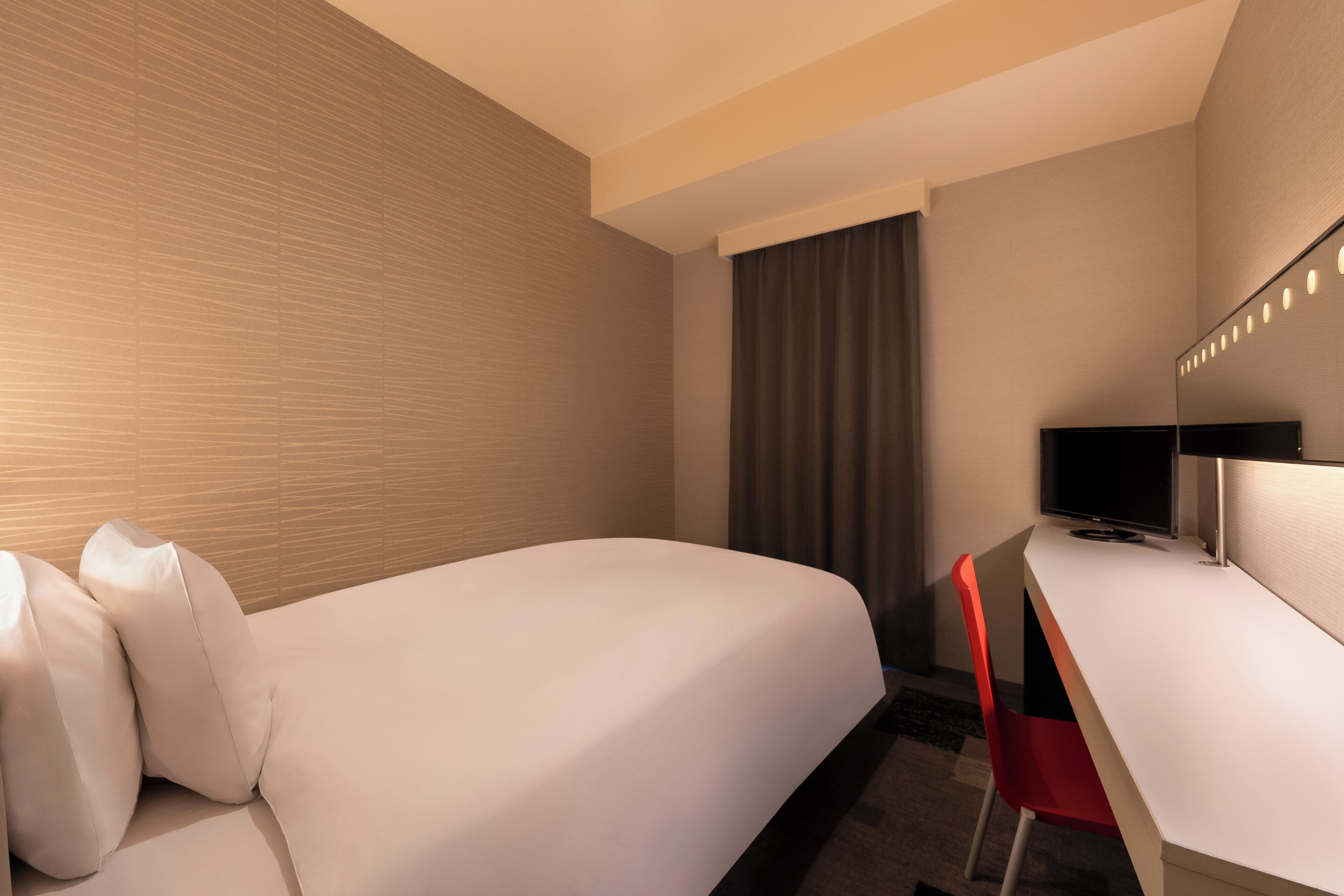 A hotel room with a bed, a desk, a television, and a mirror.