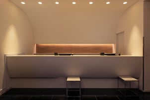 Una zona de recepción moderna con techo curvo, iluminación empotrada, un mostrador de recepción y dos pequeñas mesas.