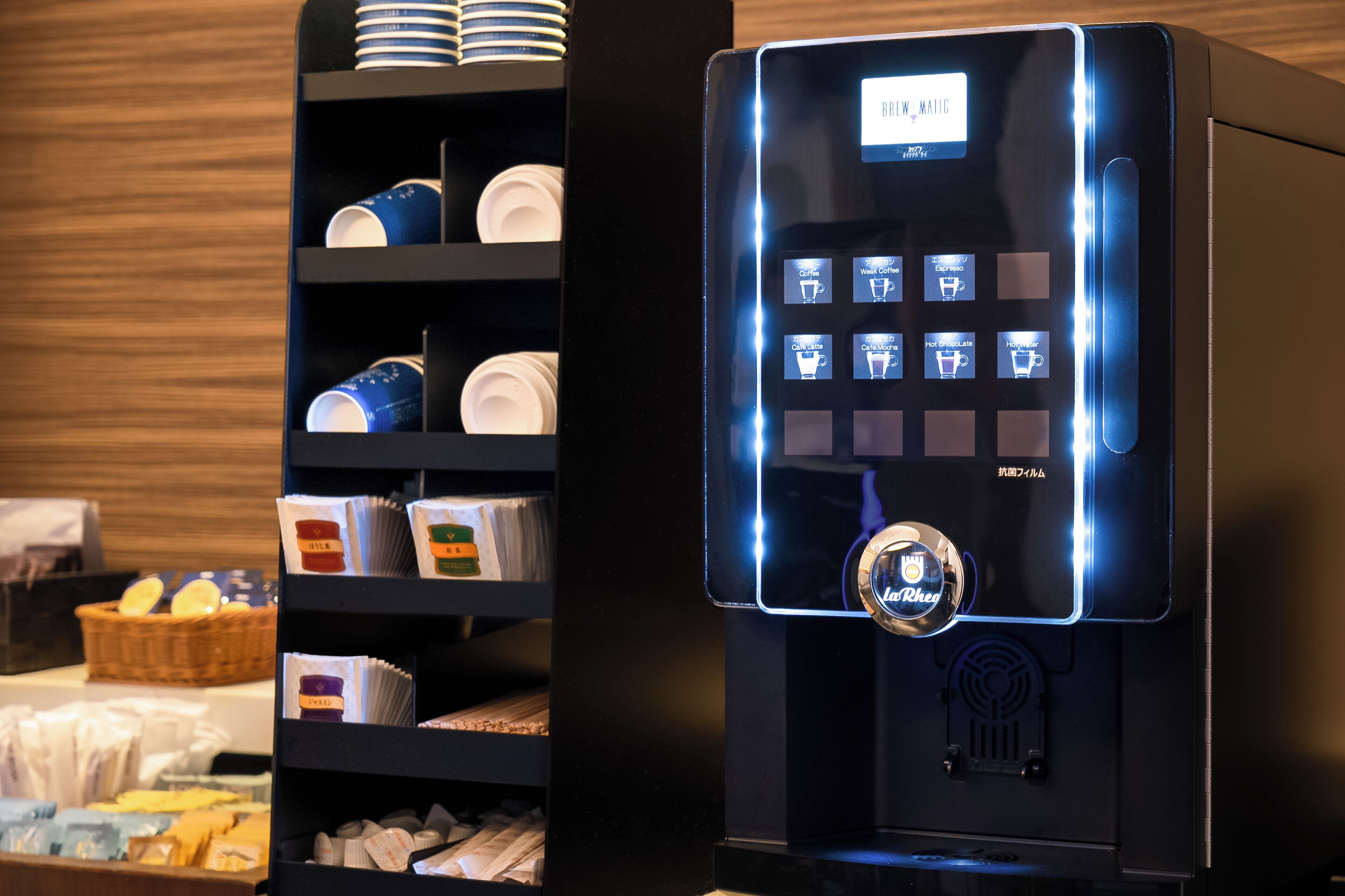 A coffee machine with a digital display and a coffee station with cups and containers.