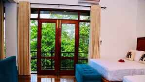 Ein Schlafzimmer mit einer großen Schiebeglasdoor, die zu einem Balkon führt, zwei Betten, einem blauen Sessel und einem blauen Hocker.