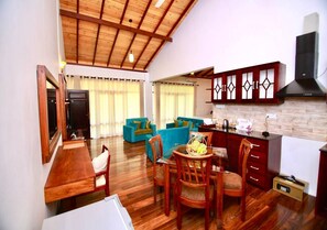 A spacious living area with a wooden dining table, blue sofas, and a kitchen with wooden cabinets and a black range hood. - The Grand Hanthana (Kandy)