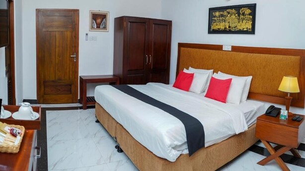 Ein Hotelzimmer mit einem großen Bett, einem Holz-Kopfteil, einem Nachttisch mit Lampe, einem Kleiderschrank und einem gerahmten Bild an der Wand.