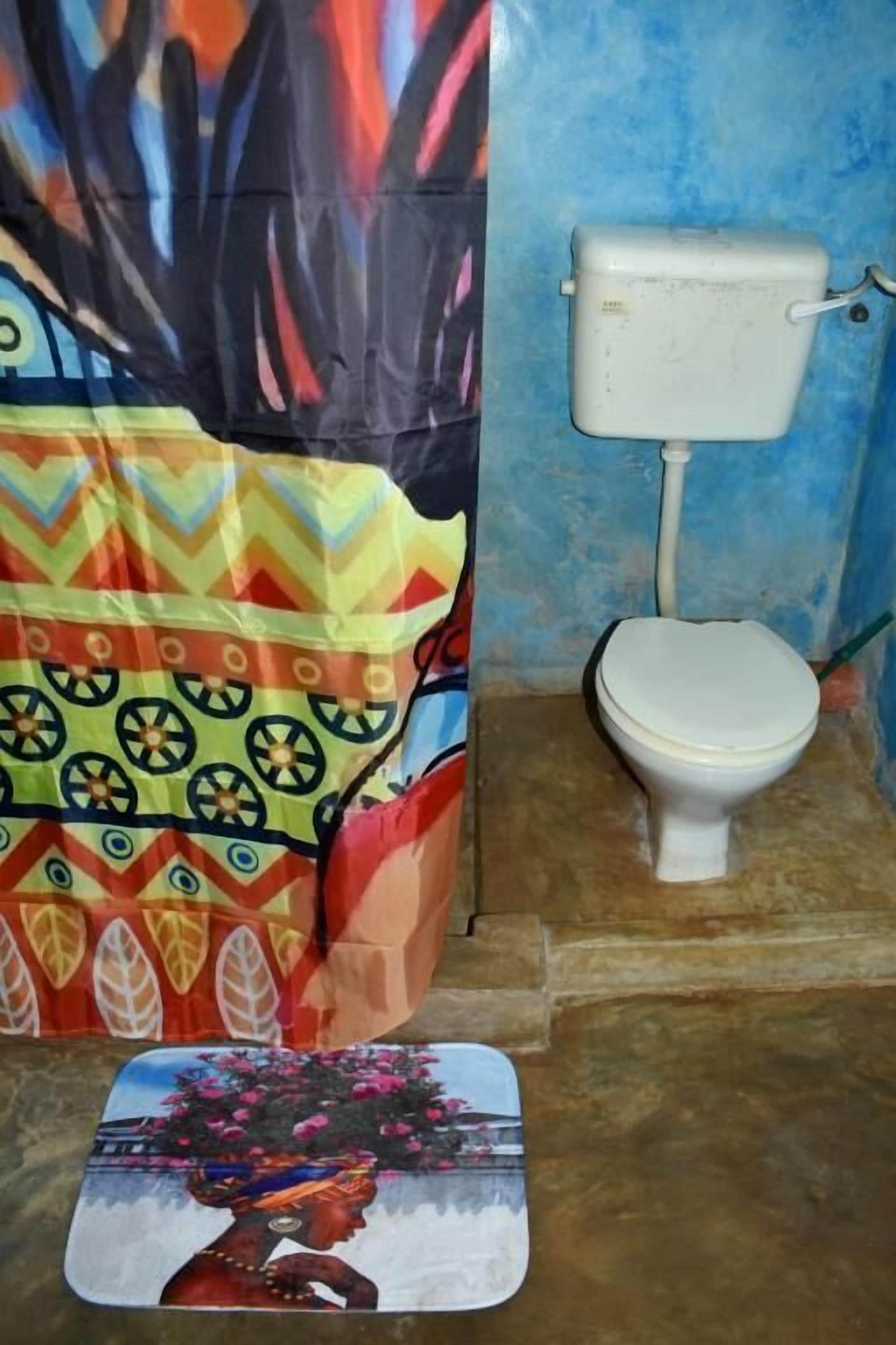 A bathroom with a white toilet, a colorful shower curtain, and a decorative mat.