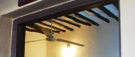 A room with a bed, a ceiling fan, a table with a lamp, and a sign that reads "SHELA".