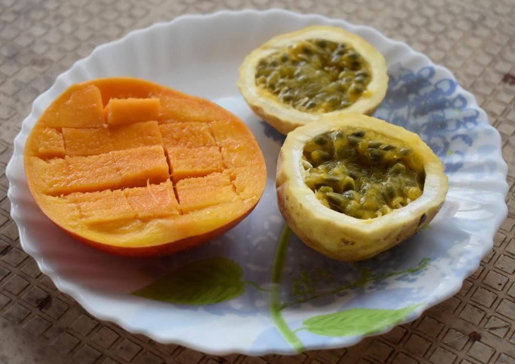 A white plate with a half-cut mango and a half-cut passion fruit.