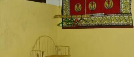 A room with a ceiling fan, a woven chair, a green plastic chair, and a decorative wall hanging.