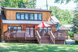 Une cabane en bois à deux étages, dotée d’une terrasse, d’un escalier et d’un parasol rouge.