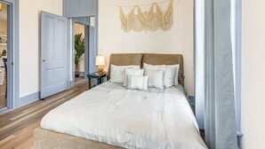 Una camera da letto con un letto grande, un comodino con una lampada e un arazzo in macramè appeso al muro.