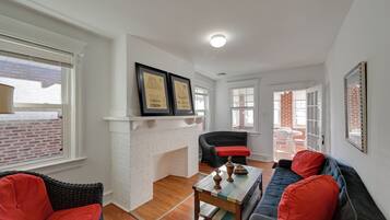 A living room with a fireplace, wicker furniture, and a sofa with red cushions.