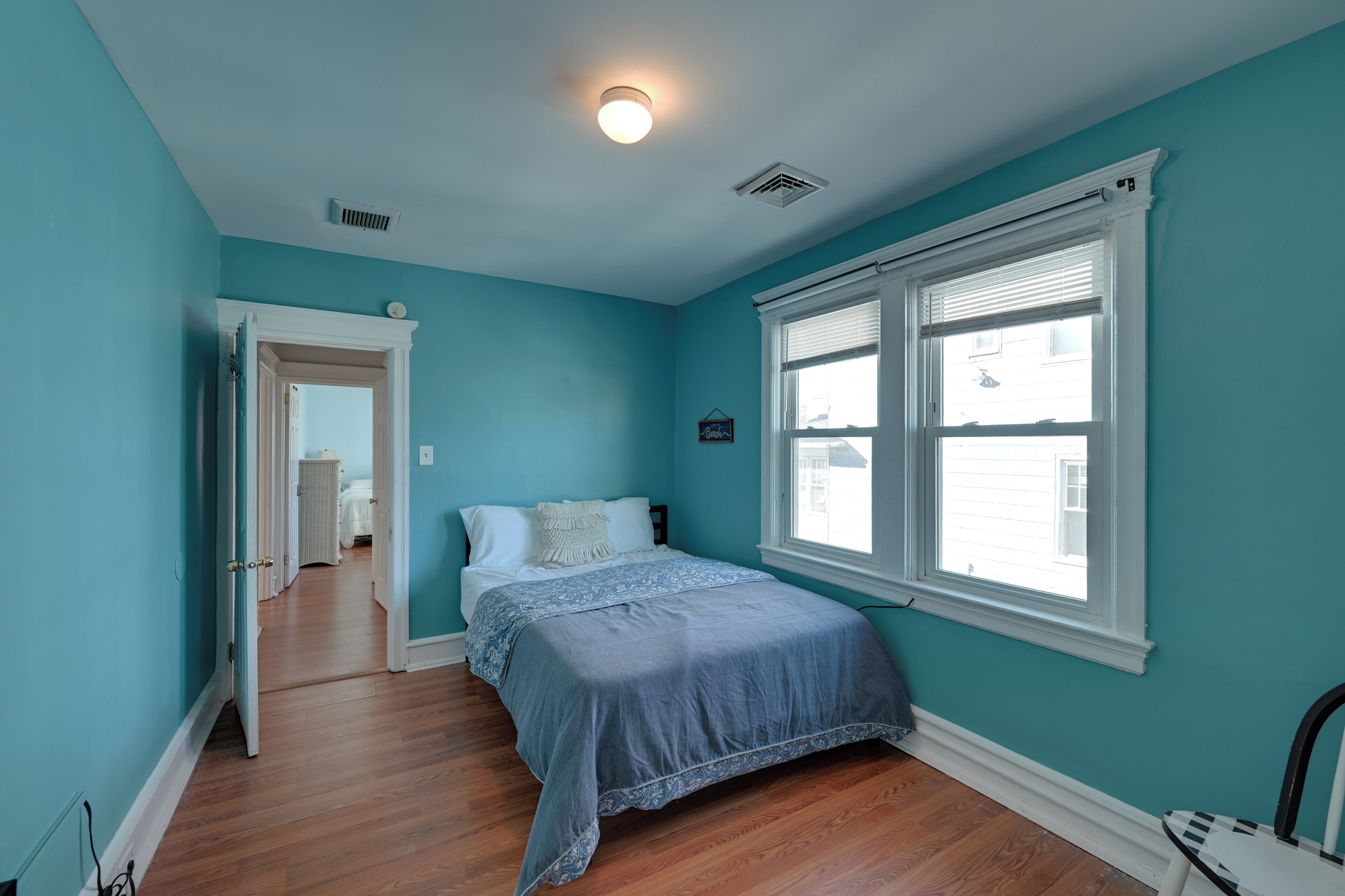 A bedroom with teal walls, a wooden floor, a bed with a blue bedspread, and a window with blinds.