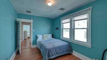 A bedroom with teal walls, a wooden floor, a bed with a blue bedspread, and a window with blinds.
