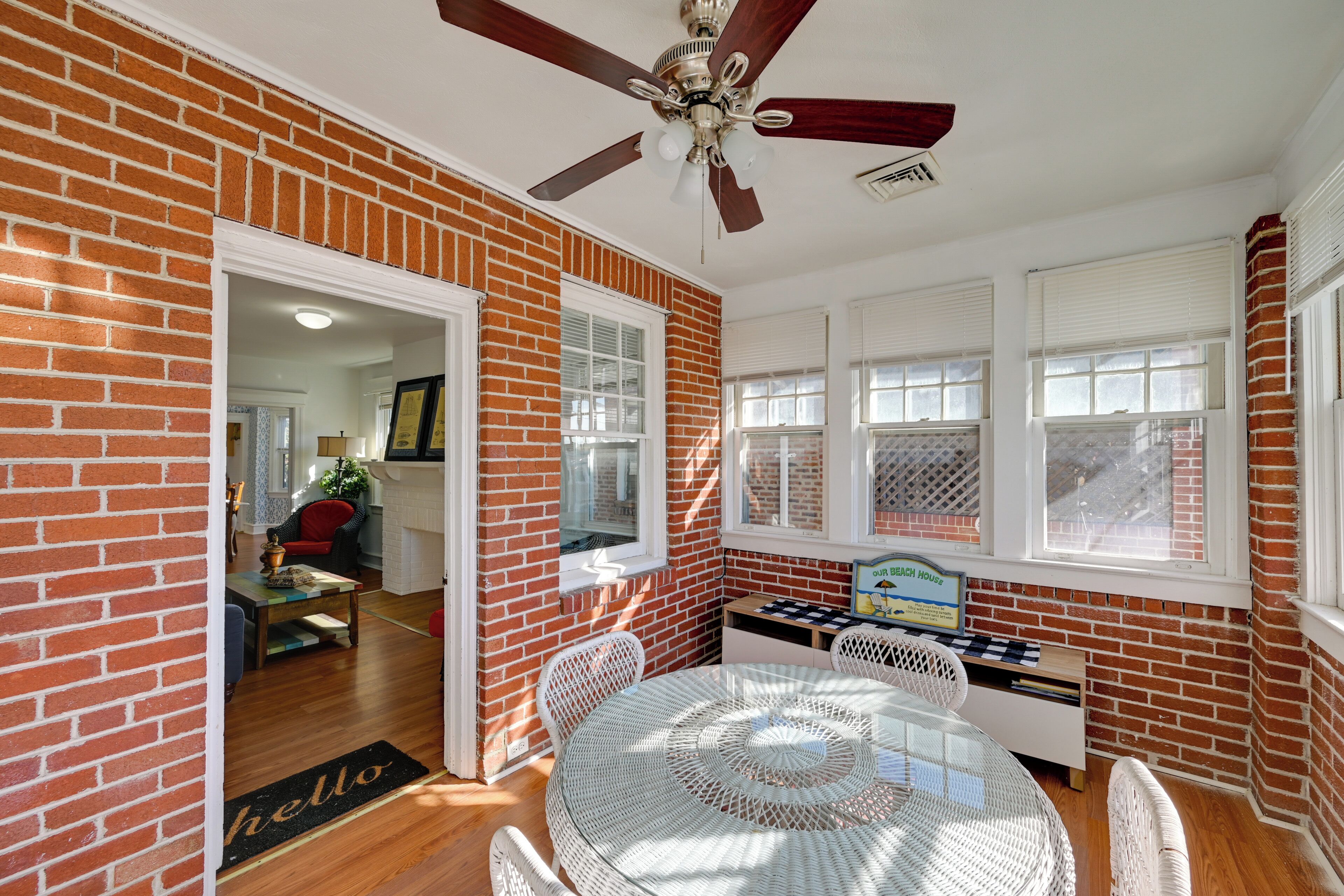 A room with a brick wall, a ceiling fan, a round table with chairs, and a door leading to another room.