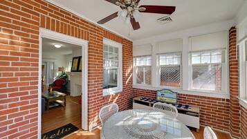 A room with a brick wall, a ceiling fan, a round table with chairs, and a door leading to another room.