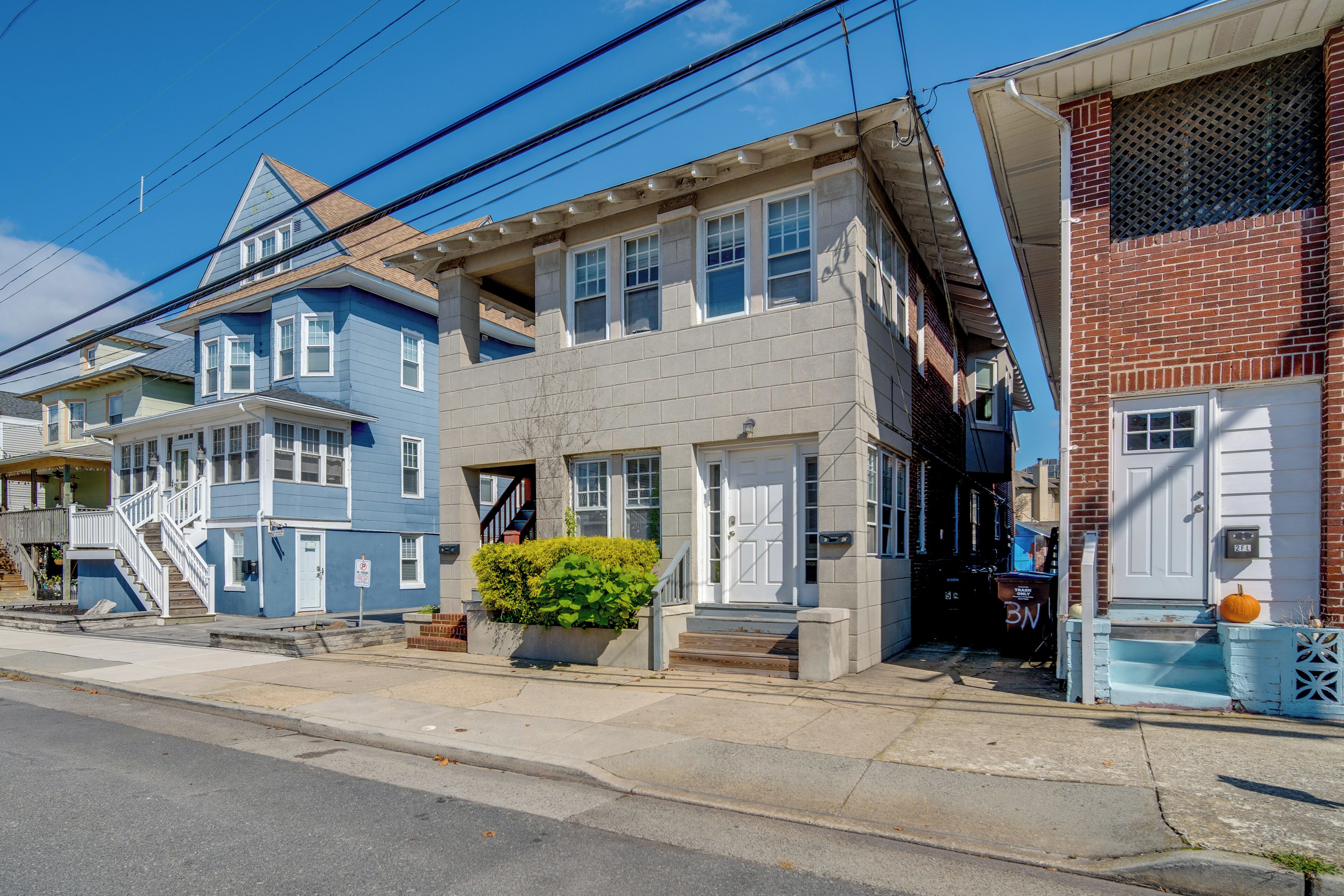 A row of residential buildings with a central two-story house featuring a front porch, a small garden, and a mailbox.