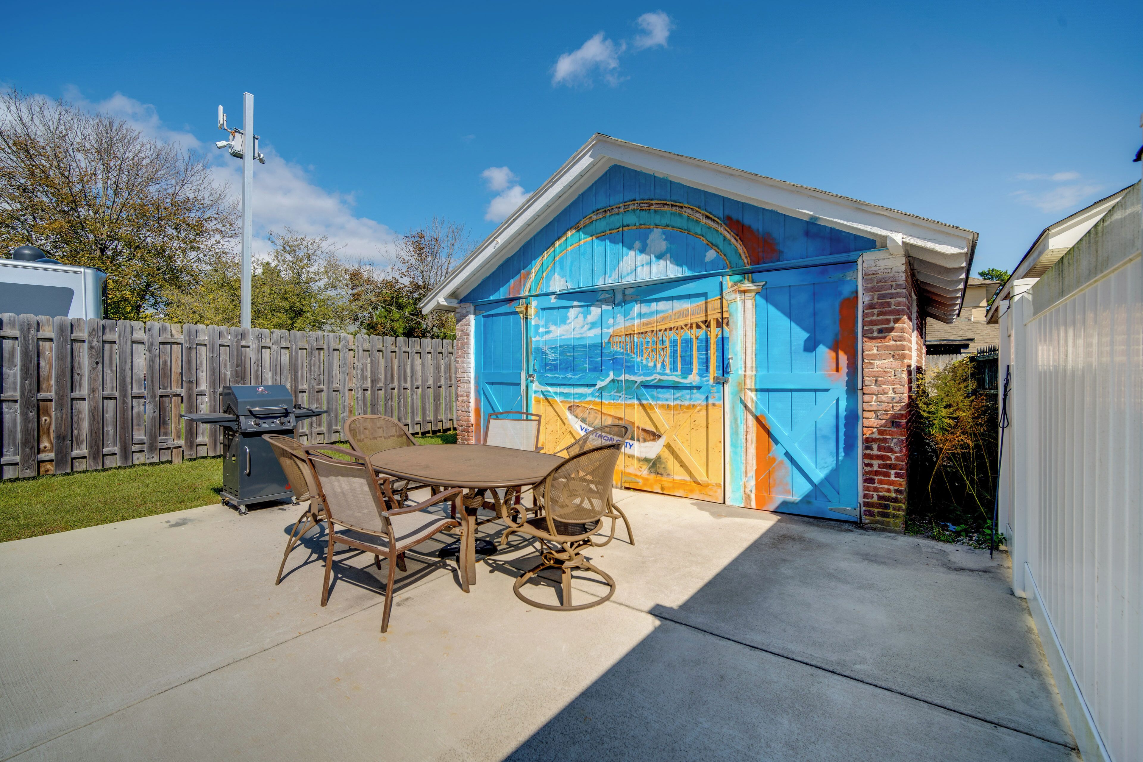 Une terrasse avec une table et des chaises, un barbecue et une fresque sur la porte du garage.