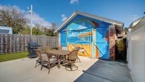 Une terrasse avec une table et des chaises, un barbecue et une fresque sur la porte du garage.