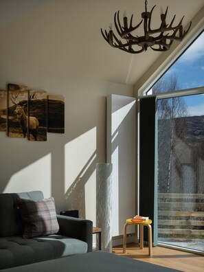 Un salon moderne doté d’une grande fenêtre, d’un canapé, d’une table basse et d’un lustre original en forme de bois de cerf.