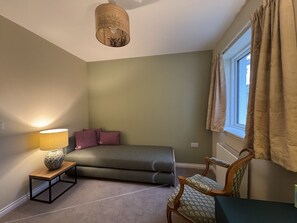 A bedroom with a bed, a bedside table with a lamp, a chair, and a window with curtains. - Sunny Ridge is a modern, open-plan, sustainable bungalow, with stunning views. (Fort Augustus)