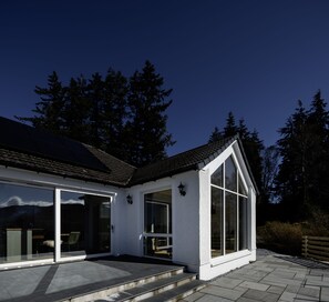 A modern house with a sloped roof, large windows, and a solar panel on the roof. - Sunny Ridge is a modern, open-plan, sustainable bungalow, with stunning views. (Fort Augustus)