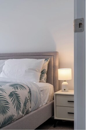 A neatly made bed with a tropical leaf pattern bedspread, a bedside lamp, and a small bedside table with drawers. - 4BR Warm & Relaxing Ripley Escape - Inspire Haven (Ripley)