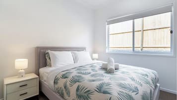 A bedroom with a bed, nightstands, and a window with a view of a wooden fence.
