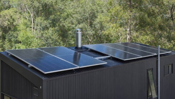 Um edifício moderno com painéis solares no telhado e uma pequena janela.