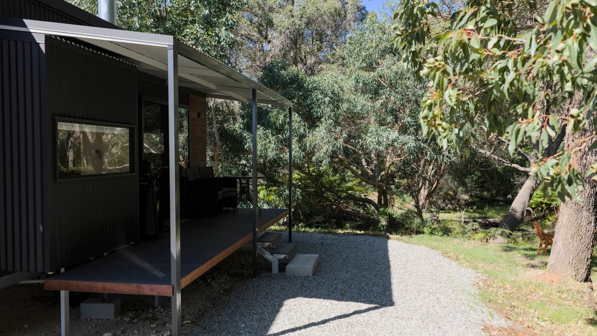 A modern building with a covered outdoor area, a gravel path, and surrounding trees.