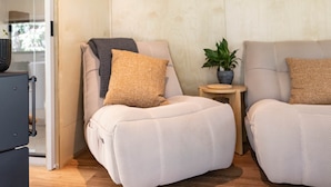 A modern room with two seating areas, a small side table with a plant, and a glass partition. - Off Grid Tiny Home  : City Escape, Unwind & Reconnect with Nature (North Dandalup)