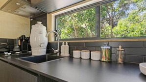 Cozinha moderna com pia embutida, cafeteira e janela com vista para árvores.
