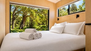 A bedroom with a large bed, white bedding, and a view of trees through a window.