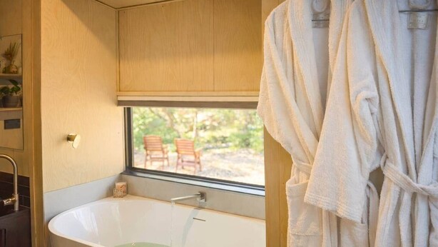 A bathroom with a bathtub, a window, and a view of outdoor chairs. - Off Grid Tiny Home Fern View: Escape the City, Unwind & Reconnect with Nature (North Dandalup)