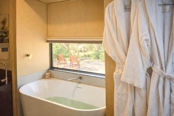 A bathroom with a bathtub, a window, and a view of outdoor chairs. - Off Grid Tiny Home Fern View: Escape the City, Unwind & Reconnect with Nature (North Dandalup)
