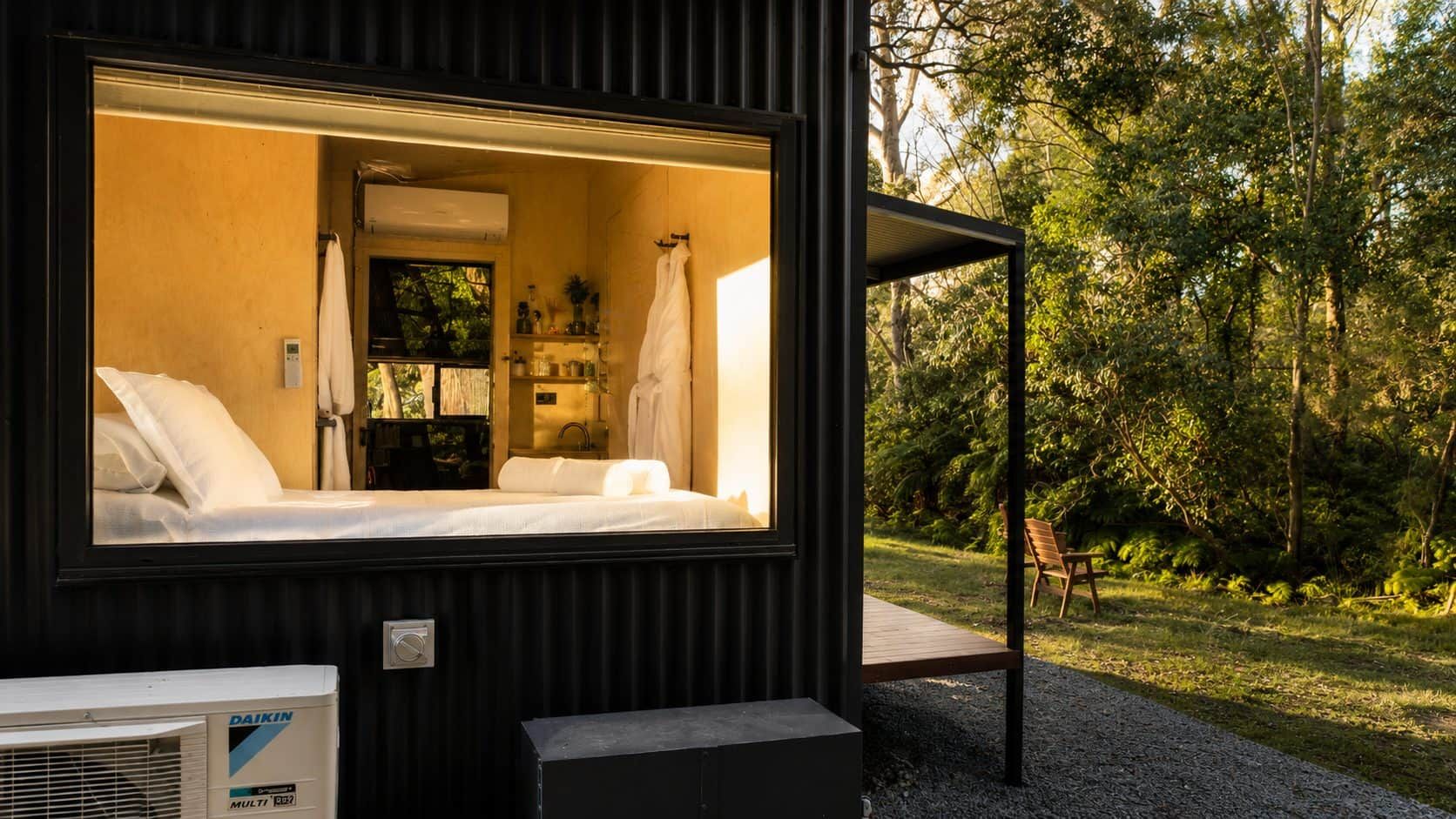 Une chambre moderne et compacte, dotée d’une grande fenêtre, d’un lit et d’un espace salle de bain visible.