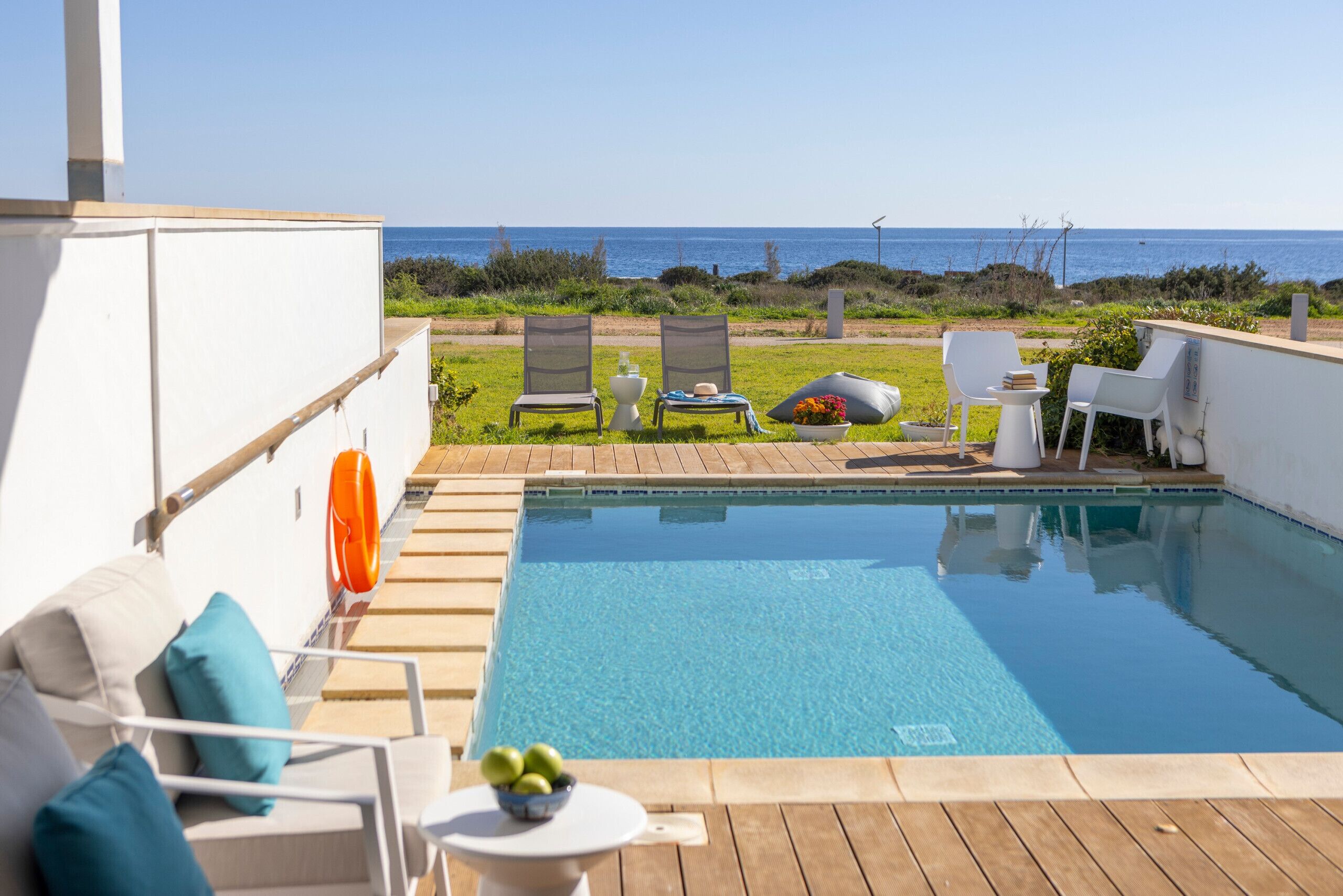 A pool area with a view of the sea, outdoor seating, and a wooden deck.