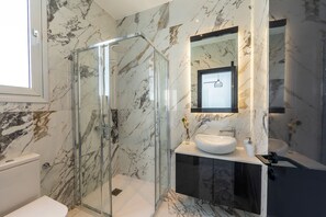 Un bagno moderno con doccia vetrata, lavandino bianco e pannello di marmo.