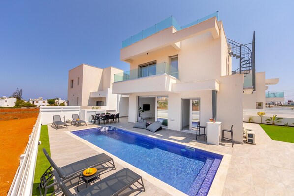 Una casa moderna su due piani con piscina, area salotto esterna e un balcone.