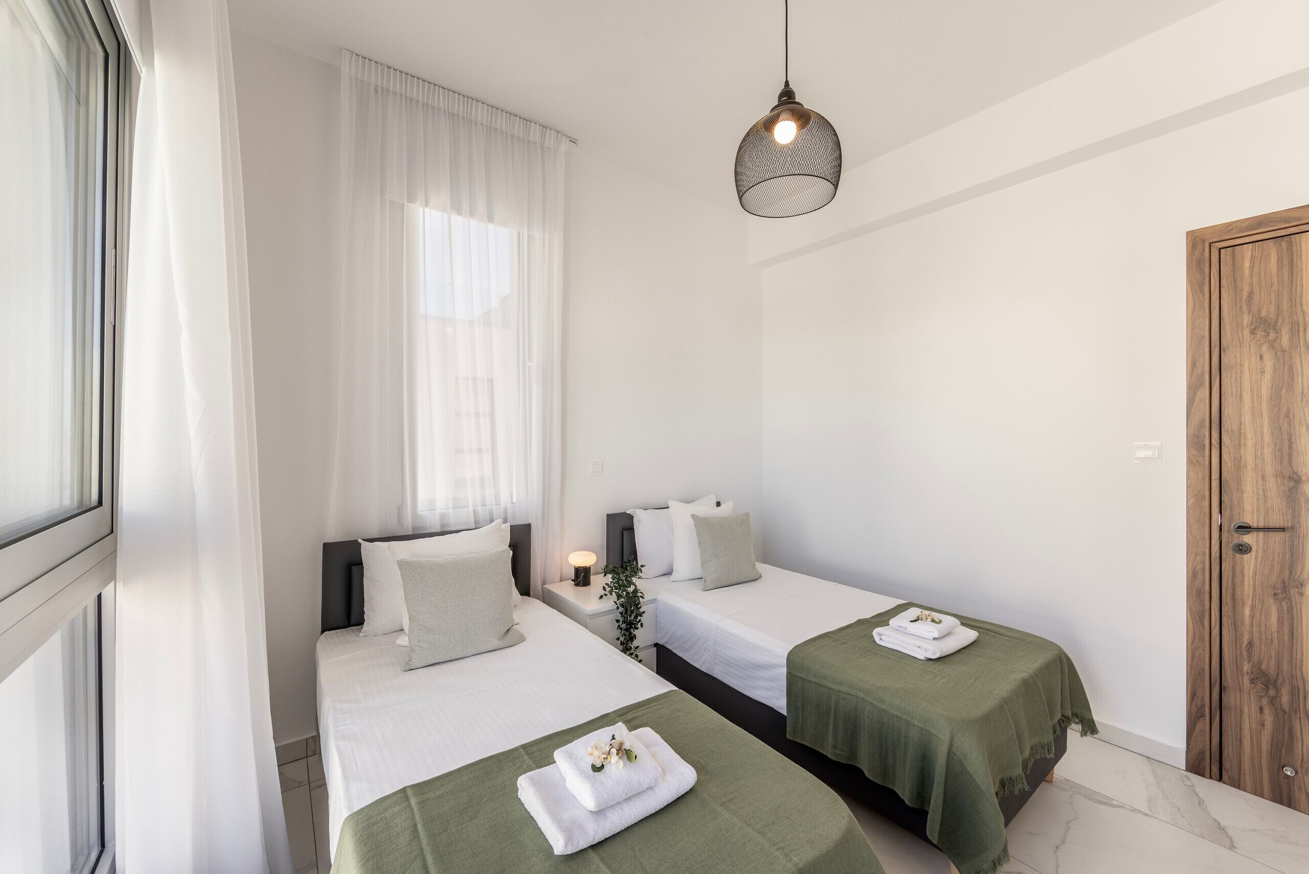 A hotel room with two beds, a wooden door, and a hanging light fixture.